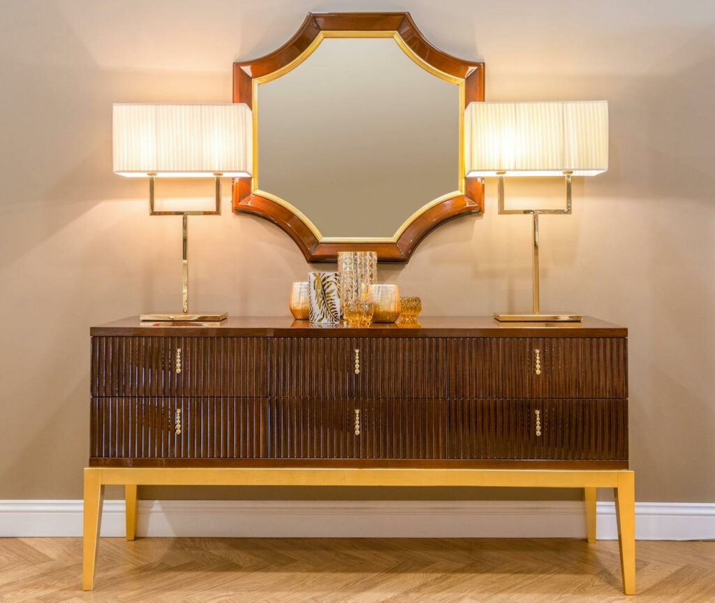 Un buffet élégant en bois massif surmonté d'un grand miroir doré et de deux lampes de table design dans un intérieur raffiné