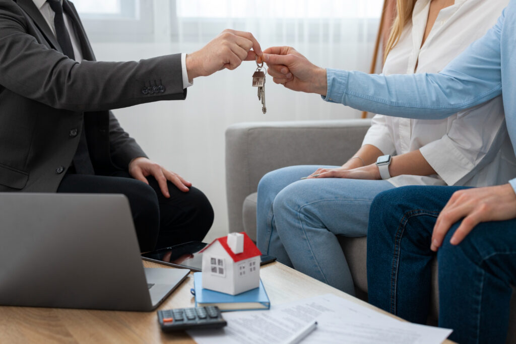 Un agent immobilier en costume remet les clés d'un logement à un couple assis sur un canapé